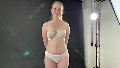 Pretty young woman in strapless bra as underwear is posing in studio with black background