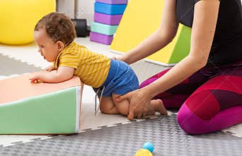 Physical therapist assisting baby with coordination exercise in rehab center for recovery after birth trauma and damage