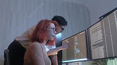 Programmers working at night analyzing code on monitors in a modern office
