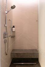 Modern shower stall with stone wall, handheld shower head, bench, and glass door in neutral bathroom interior
