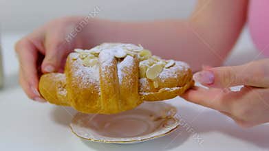 Female hand holding almond croissant dusted with powdered sugar before taking a bite during cozy breakfast close up