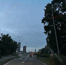 Evening traffic on wet city road with high rise office towers, streetlights