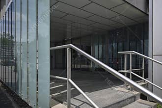 Modern Office Building Entrance with Glass Panels and Metal Handrails Reflecting Urban Environment