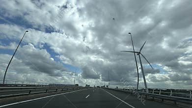 Empty highway bridge with wind turbine under dramatic cloudy sky, leading toward