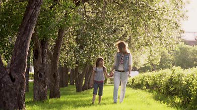 Mother walks with her daughter along the avenue of apple trees. The little girl is holding her mother by the hand. Child