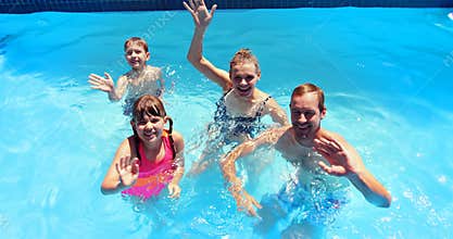 Portrait of happy family waving hand in swimming pool