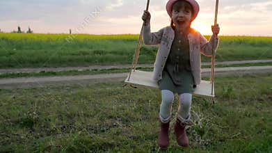 Portrait cute girl shakes on hanging from tree swing, children on swing, female kid swaying, happy little child have fun