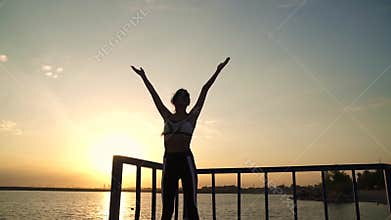 20s girl is doing breathing exercises at dawn on the beach. Beautiful young woman in sportswear practicing yoga outdoors