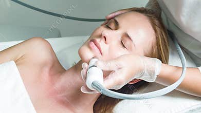 Skillful beautician treating female face by special equipment