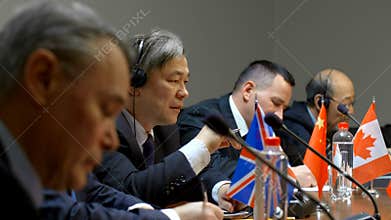 Diverse group of businessmen in suits discussing at international conference or meeting in modern congress hall.
