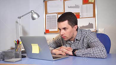 A man who looks in the laptop is surprised by what is happening on the Internet