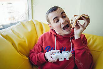 Funny young man playing video game on the gaming console and eat delicious pizza. Looking for pizza.
