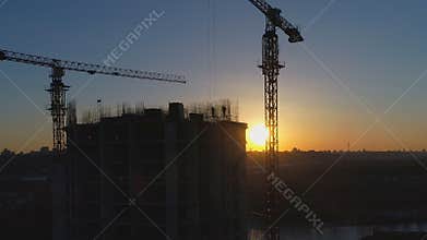 Aerial shot of construction site with cranes and workers at sunset