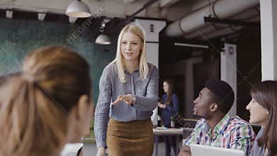 Beautiful blonde woman manager giving direction to multiethnic team. Creative business meeting at modern hipster office.