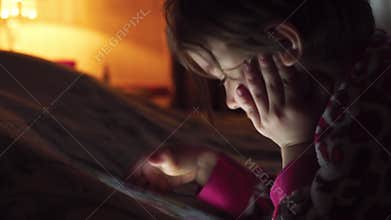 Closeup of a Little cute girl in full darkness watching tablet