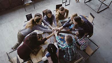 Top view of business team working at trendy loft office. Young mixed race group of people puts palm together on centre.