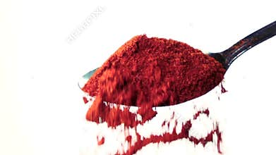 Red chili powder falling from the iron spoon. White background. Slow motion
