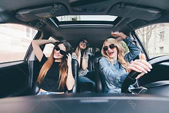 Three girls driving in a convertible car and having fun, listen music and dance