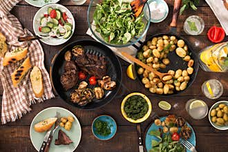 Dinner table with grilled steak, vegetables, potatoes, salad, sn