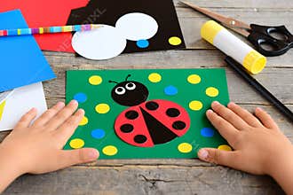 Child made a ladybird from colored paper. Summer card with paper ladybug, stationery on a wooden table. Simple paper circle crafts