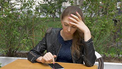 Sad beautiful girl sitting at a table in a cafe. Reads sms on a smartphone. Sadness and longing, hopelessness. Close-up