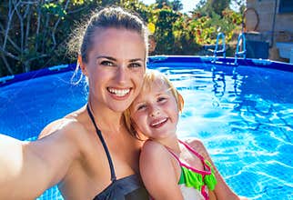 Smiling mother and daughter in swimming pool taking selfie