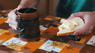 Man is spreading butter on a bread next to a cup of hot coffee