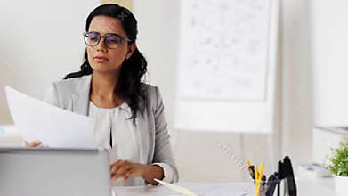 Businesswoman with laptop and papers at office