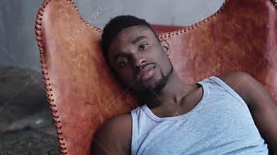 Portrait of young handsome african man sitting on the leather chair and looking at camera. Serious model male.