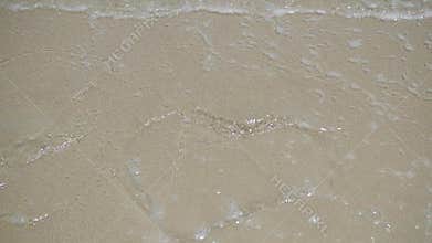 A sea wave is washing away the pattern on the sand with a sunny day