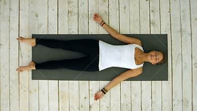 Attractive young woman working out at home, doing yoga exercise, lying in Shavasana Corpse or Dead Body Pose , resting