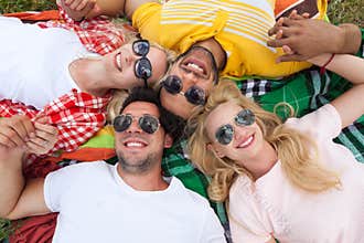 Happy people group young friends lying down on picnic blanket outdoor