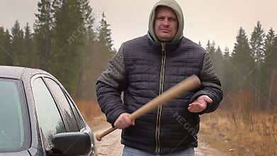 Aggressive man with a baseball bat near car