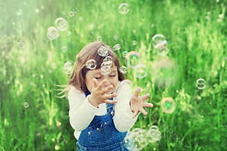 Cute little girl playing with soap bubbles on the green lawn outdoor, happy childhood concept, child having fun