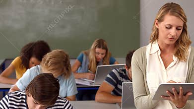 Students taking notes and teacher using tablet pc