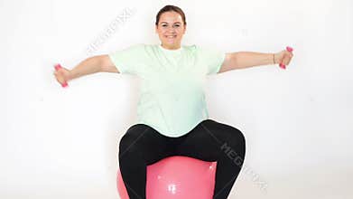 Fat woman making exercises with dumbbells on a fitness ball