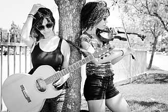 Woman violinist and woman guitarist leaning against tree
