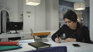 A woman working at the computer, taking notes on a sheet, crumples and throws