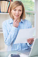 Concerned Woman In Home Office Looking At Letter