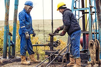 Oil workers check oil pump. Roustabouts doing dirty and dangerous work