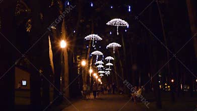 Walking people in the alley and the LED lamps in the form of umbrellas in the park in the evening