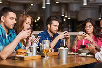 Friends with smartphones dining at restaurant