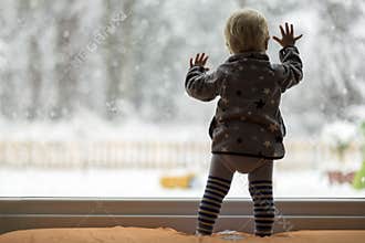 Toddler child standing in front of a big window leaning against