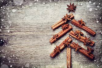 Christmas card with Christmas fir tree made from spices cinnamon sticks, anise star and cane sugar on rustic wooden background