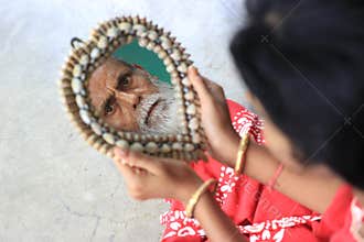 An old man s face is reflecting from the mirror but a girl is holding that mirror.
