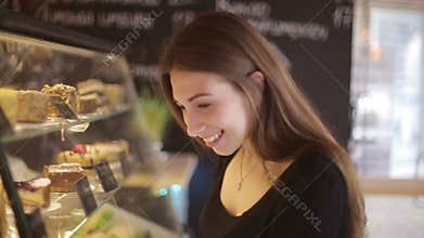 Beautiful female customer shopping showcase in a bakery store pointing at the dessert she is buying