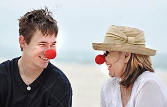 Mother and son having fun laughing celebrating red nose day on beautiful beach holiday