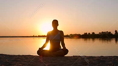 Woman meditating in pose lotus over orange sun
