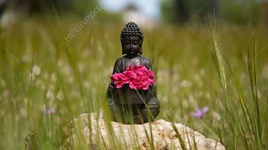 Buddha figurine with red flowers in the middle of green meadow
