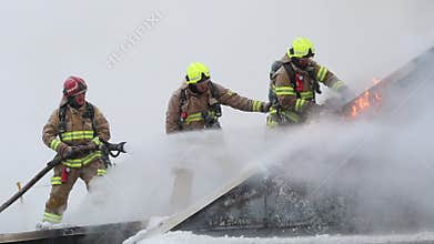 Fire fighters stand and walk on the roof of apartment building.